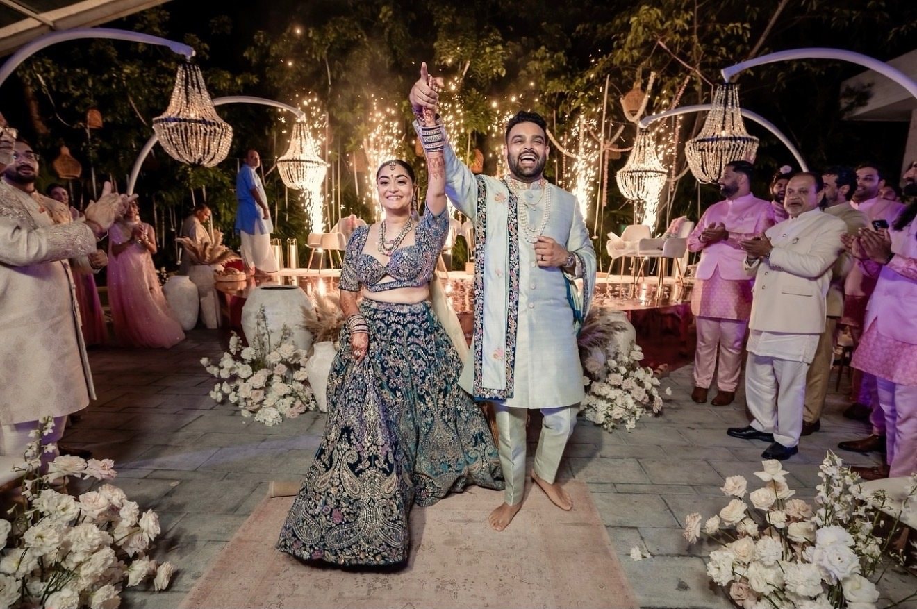 A couple dances into an evening celebration under crystal chandeliers and white floral arches as guests cheer them on.